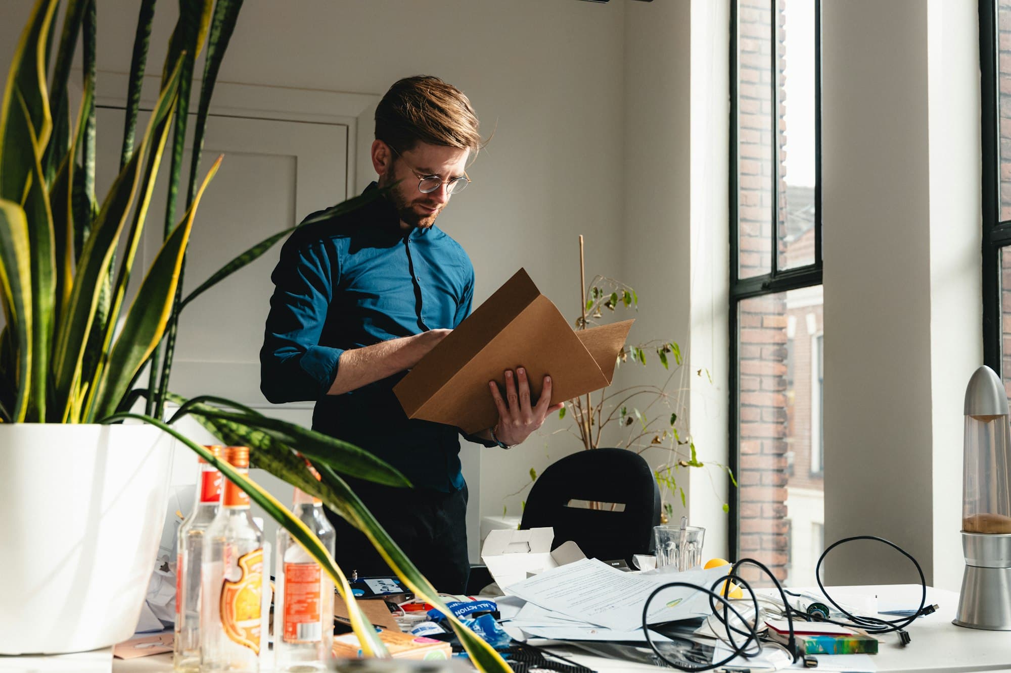 A business owner standing over a desk covered in paperwork, holding a folder