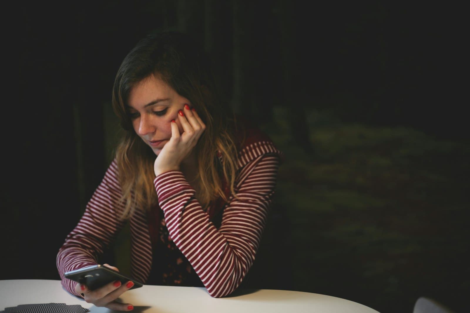 Une femme seule à une table, la joue dans la main, son téléphone posé devant elle, qui attend un message