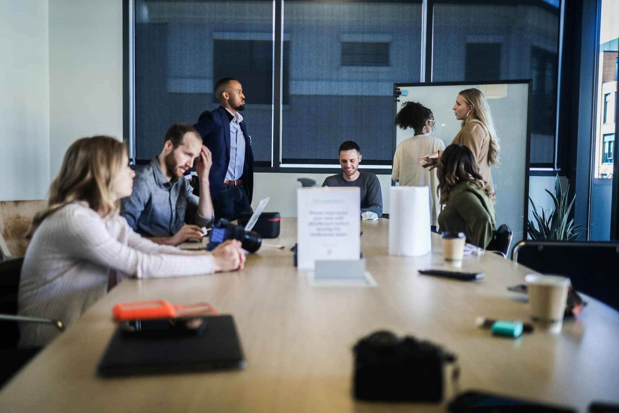 A meeting room where one person stands to explain while the others sit with their documents