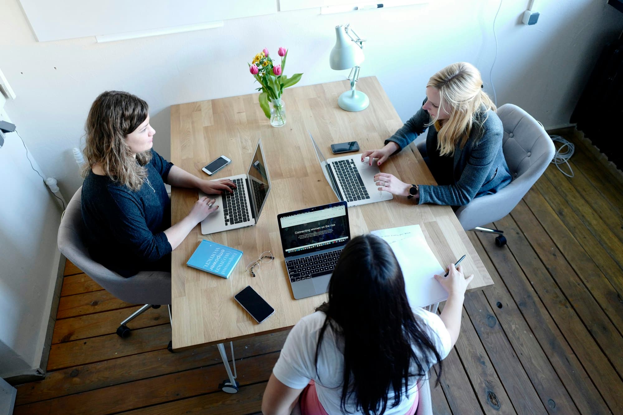 Three women around a table, each in front of her own laptop, seen from above