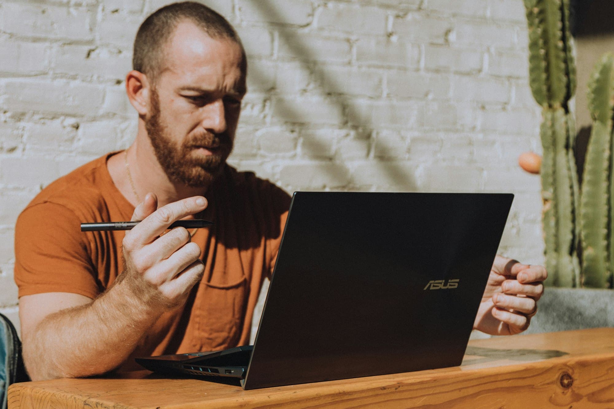 A man frowning at his laptop, pen in hand